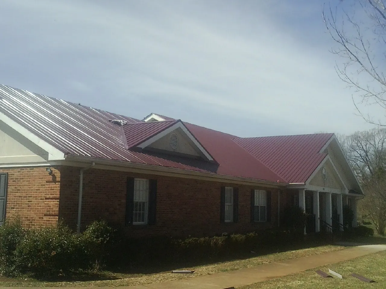 Red metal roof with gabled entries on a long brick building, from a Hail Damage Roof Repair job in Braceville