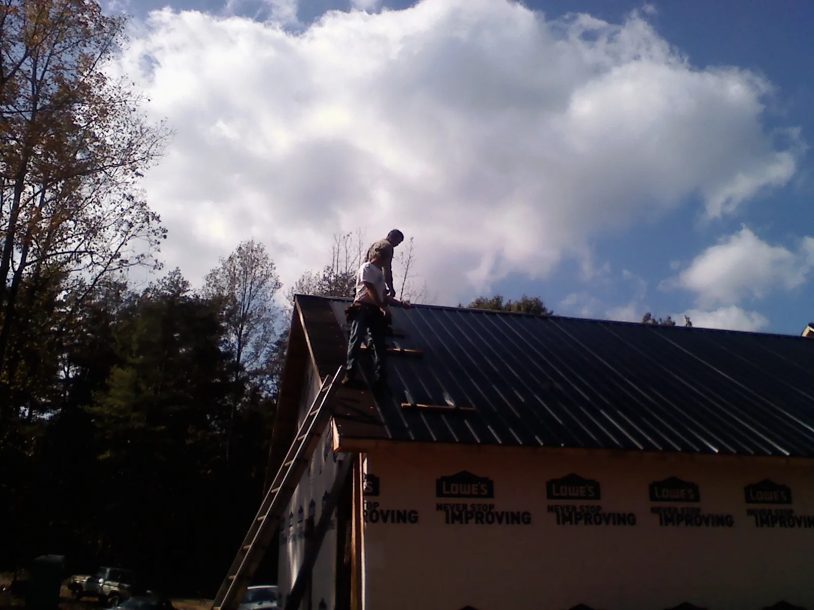 Roofer fastening dark metal panels high against a cloudy sky, from a Roof Inspection job in Braceville