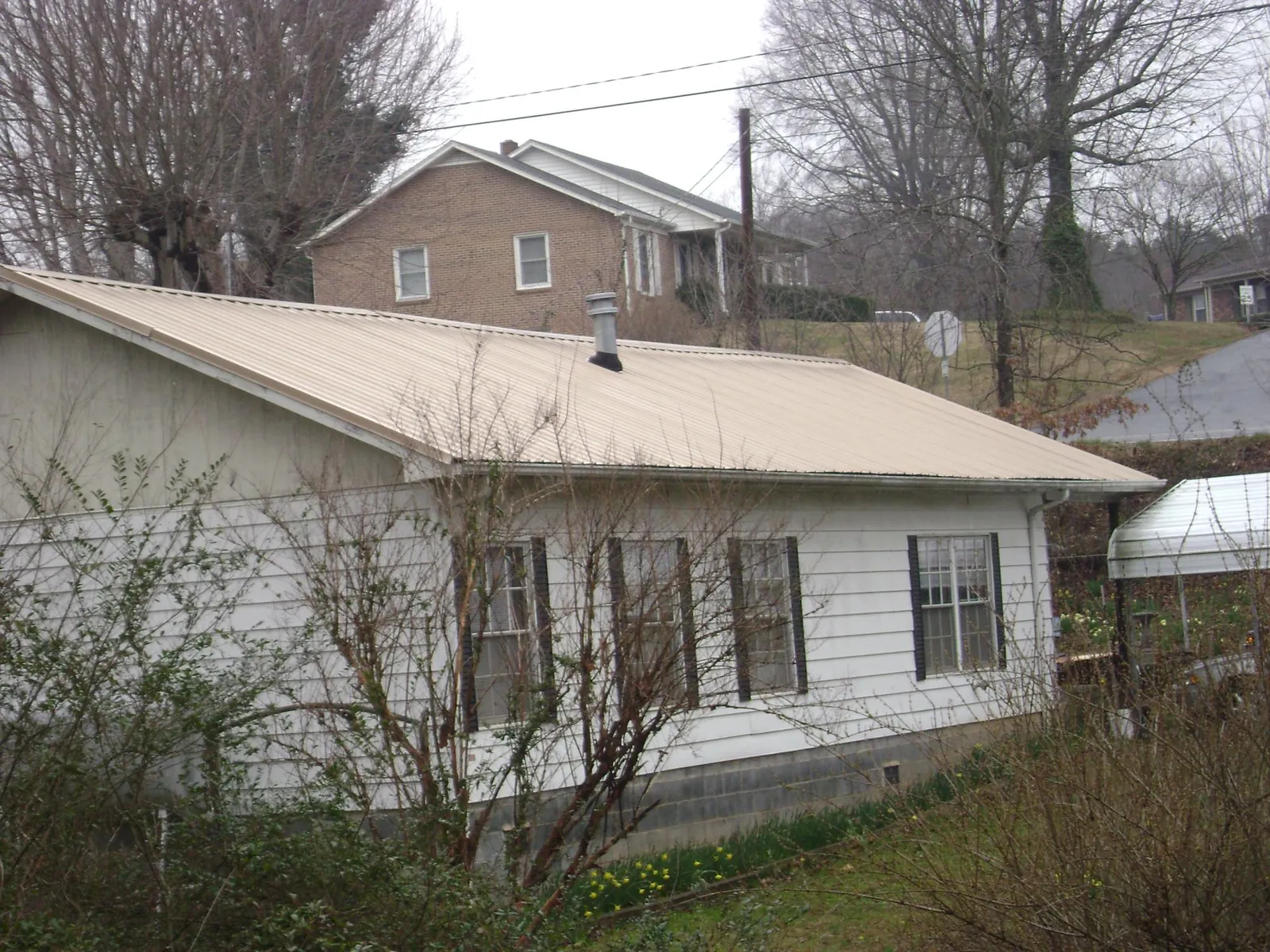 Tan metal roof on a white sided house set into a hillside — Commercial Roofing by Roofing Brothers in Braceville